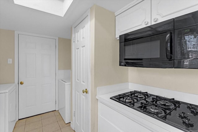 kitchen with black appliances, washer / clothes dryer, white cabinetry, and light tile patterned floors