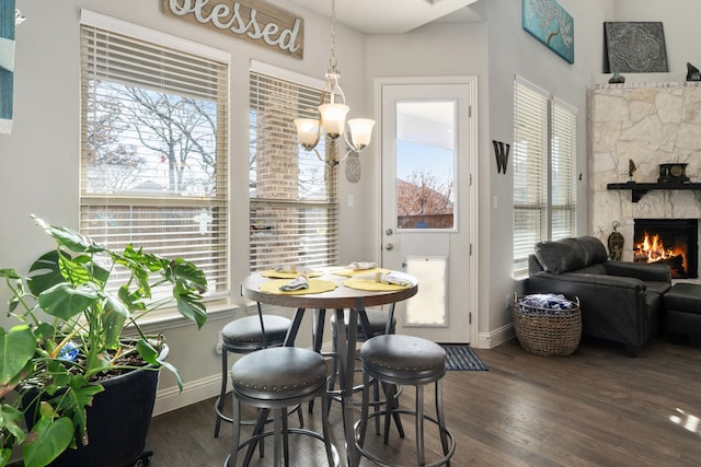 dining area with dark hardwood / wood-style floors, a stone fireplace, and an inviting chandelier