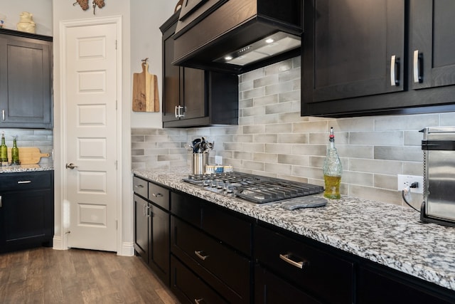 kitchen with stainless steel gas cooktop, light stone counters, dark hardwood / wood-style flooring, backsplash, and custom exhaust hood