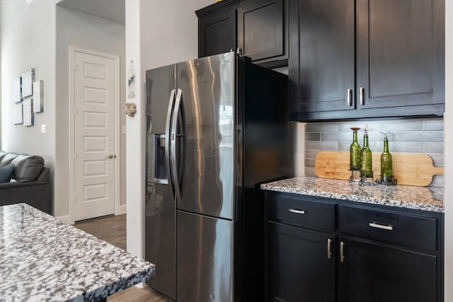 kitchen featuring decorative backsplash, stainless steel fridge with ice dispenser, light stone countertops, and dark wood-type flooring