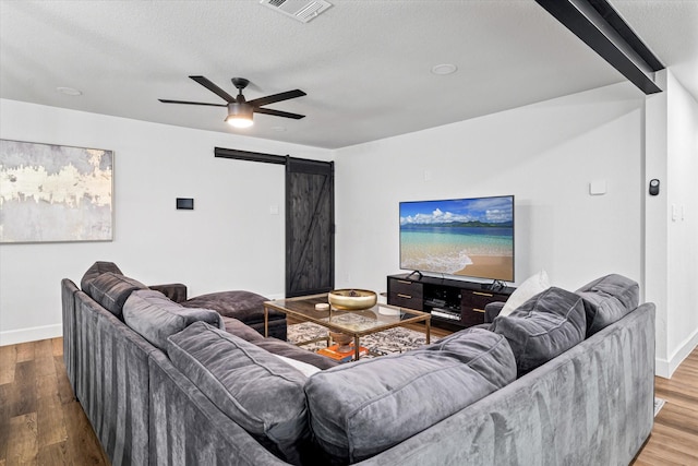 living room featuring ceiling fan, a barn door, wood-type flooring, and a textured ceiling