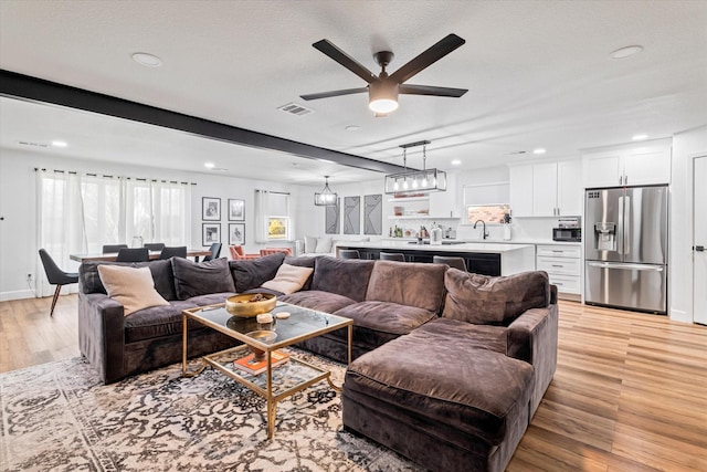 living room featuring beam ceiling, ceiling fan, sink, a textured ceiling, and light wood-type flooring