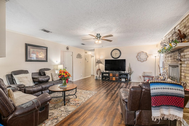 living room with ceiling fan, dark hardwood / wood-style flooring, crown molding, a textured ceiling, and a fireplace