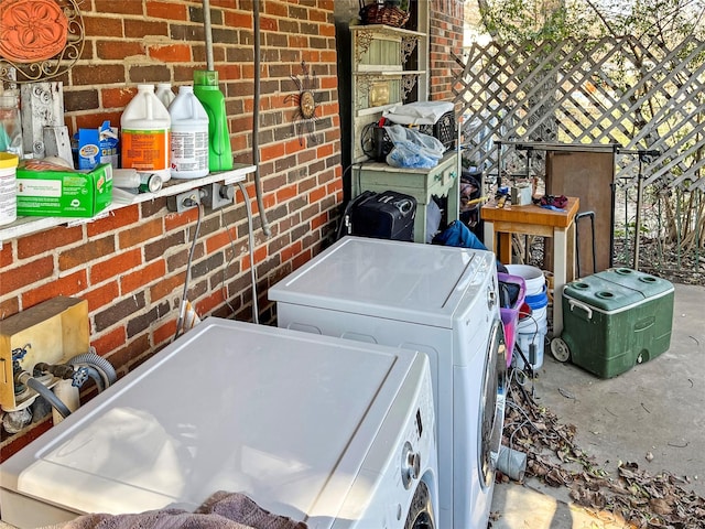 clothes washing area with washer and dryer and brick wall