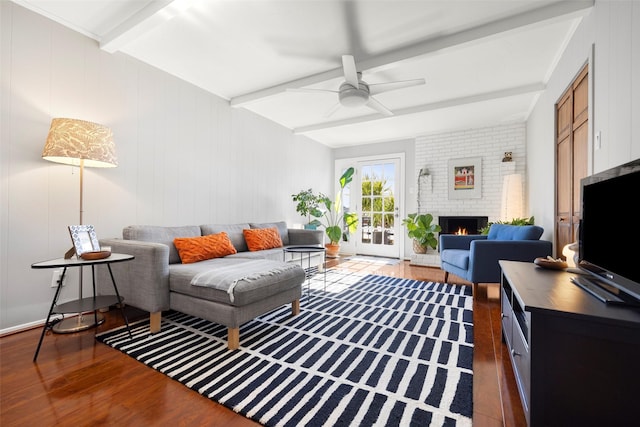 living room featuring beamed ceiling, a brick fireplace, ceiling fan, and dark wood-type flooring