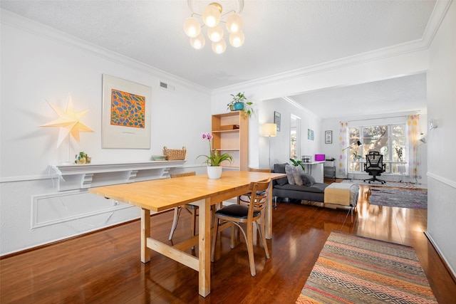 dining room featuring a textured ceiling, dark wood-type flooring, an inviting chandelier, and ornamental molding