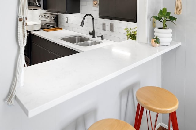 kitchen with decorative backsplash, kitchen peninsula, sink, stainless steel electric range oven, and a breakfast bar area