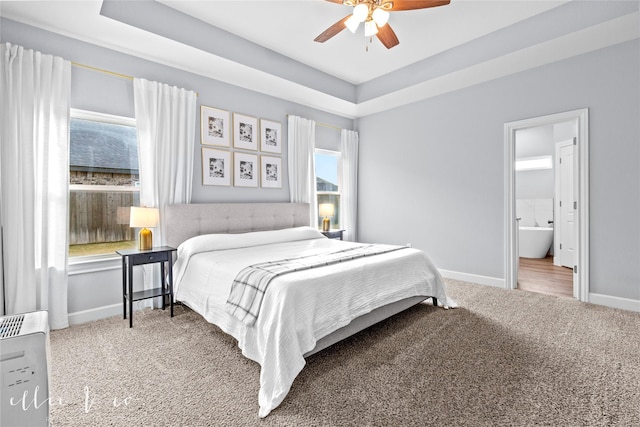 bedroom featuring carpet flooring, ceiling fan, ensuite bathroom, and a tray ceiling