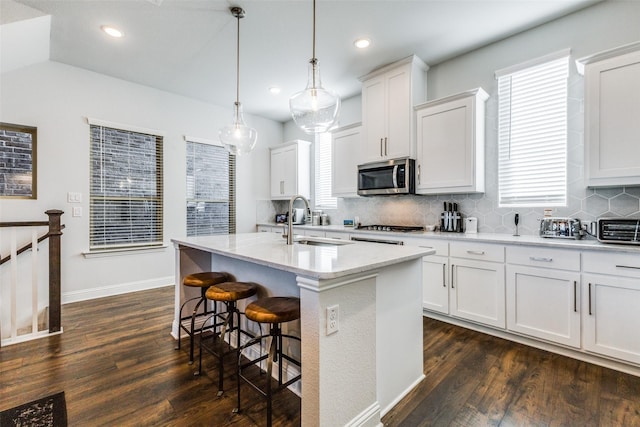 kitchen featuring white cabinets, sink, an island with sink, decorative light fixtures, and stainless steel appliances