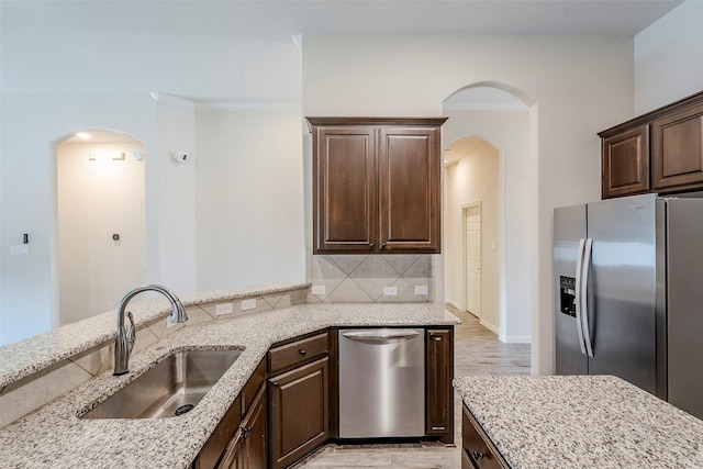 kitchen with appliances with stainless steel finishes, decorative backsplash, sink, light stone counters, and dark brown cabinets