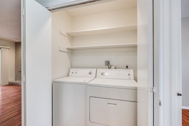 clothes washing area featuring washer and clothes dryer, brick wall, hardwood / wood-style floors, and a textured ceiling