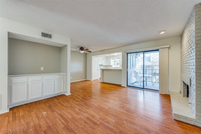 unfurnished living room featuring a textured ceiling, light hardwood / wood-style floors, a brick fireplace, and ceiling fan