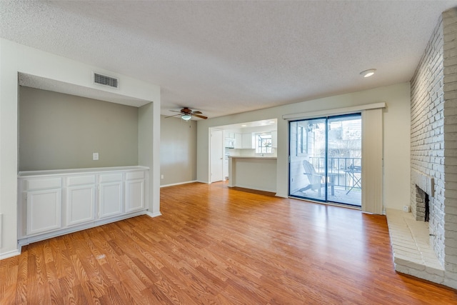 15151 Berry Trl Unit 1104, Dallas, TX 75248 - unfurnished living room with light wood finished floors, a textured ceiling, visible vents, a ceiling fan, and a brick fireplace