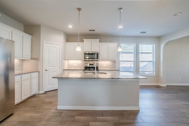 kitchen with decorative light fixtures, stainless steel appliances, and a kitchen island with sink