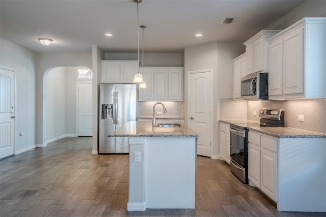 kitchen featuring a kitchen island with sink, white cabinets, hanging light fixtures, sink, and stainless steel appliances