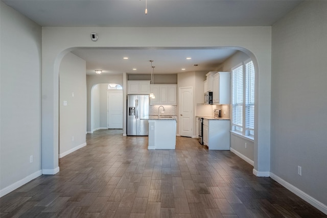 kitchen featuring decorative light fixtures, white cabinetry, an island with sink, and appliances with stainless steel finishes