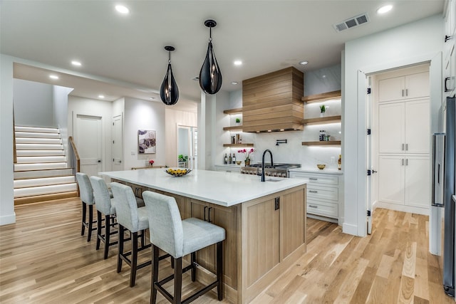 kitchen with a kitchen breakfast bar, an island with sink, light hardwood / wood-style floors, custom range hood, and stainless steel refrigerator