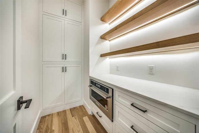 kitchen with oven, light stone counters, white cabinetry, and light wood-type flooring