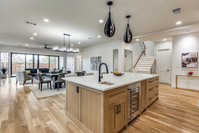 kitchen featuring ceiling fan with notable chandelier, hanging light fixtures, sink, an island with sink, and beverage cooler