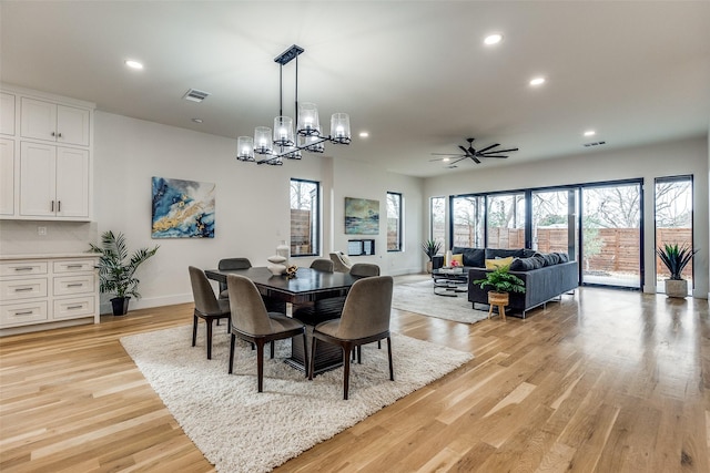 dining space with ceiling fan with notable chandelier and light wood-type flooring