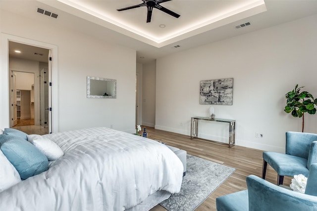 bedroom with light wood-type flooring, a raised ceiling, and ceiling fan