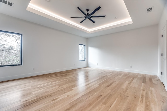 unfurnished room featuring a tray ceiling, ceiling fan, plenty of natural light, and light hardwood / wood-style flooring