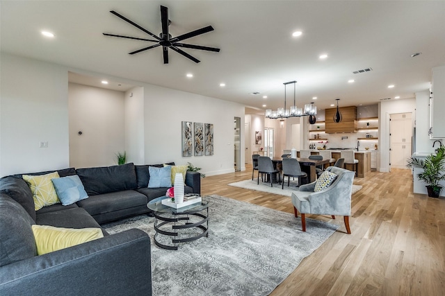 living room with ceiling fan with notable chandelier and light wood-type flooring