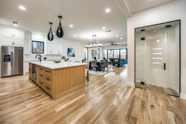 kitchen featuring white cabinetry, sink, a large island, stainless steel fridge with ice dispenser, and decorative light fixtures