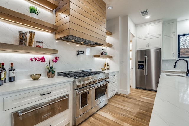 kitchen featuring white cabinetry, sink, light stone counters, premium range hood, and appliances with stainless steel finishes