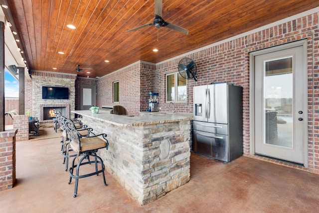 kitchen featuring a fireplace, wood ceiling, stainless steel refrigerator with ice dispenser, and brick wall