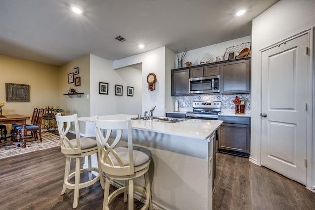 kitchen with a center island with sink, sink, dark hardwood / wood-style flooring, appliances with stainless steel finishes, and dark brown cabinets