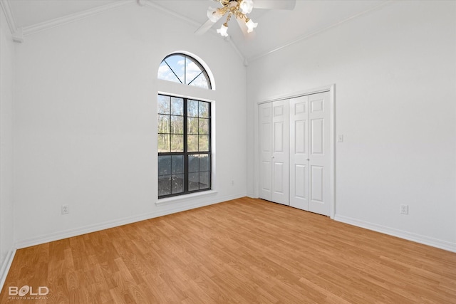 unfurnished bedroom featuring ceiling fan, crown molding, high vaulted ceiling, light hardwood / wood-style floors, and a closet