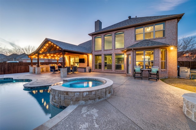 back house at dusk with outdoor lounge area, a swimming pool with hot tub, a patio area, and exterior kitchen