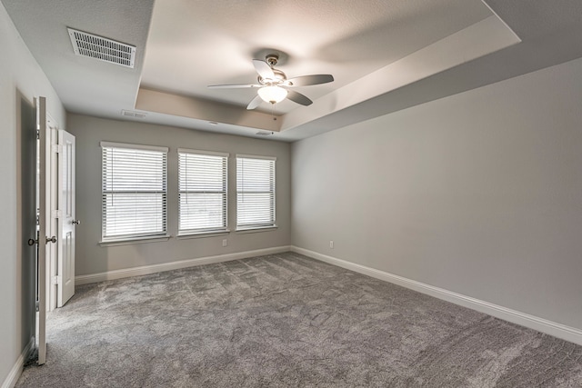 carpeted spare room with a tray ceiling and ceiling fan