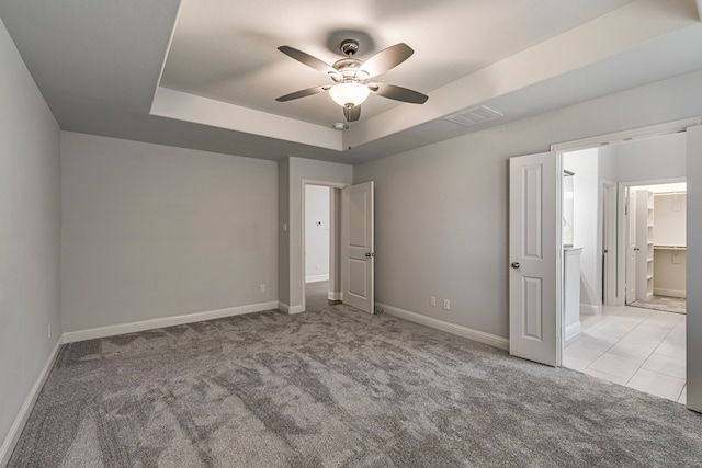 unfurnished bedroom featuring a spacious closet, light colored carpet, a raised ceiling, and ceiling fan