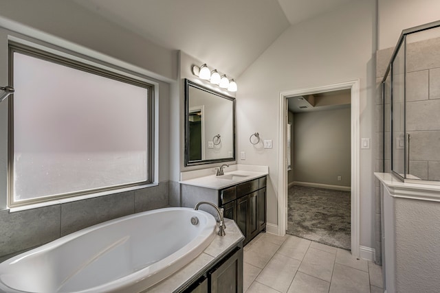 bathroom with tile patterned flooring, vanity, a relaxing tiled tub, and vaulted ceiling