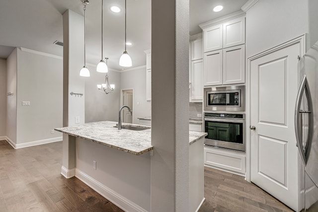 kitchen with sink, appliances with stainless steel finishes, white cabinetry, hanging light fixtures, and light stone countertops