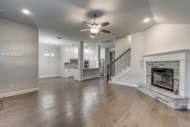 unfurnished living room featuring dark hardwood / wood-style flooring, lofted ceiling, a fireplace, ceiling fan with notable chandelier, and ornamental molding