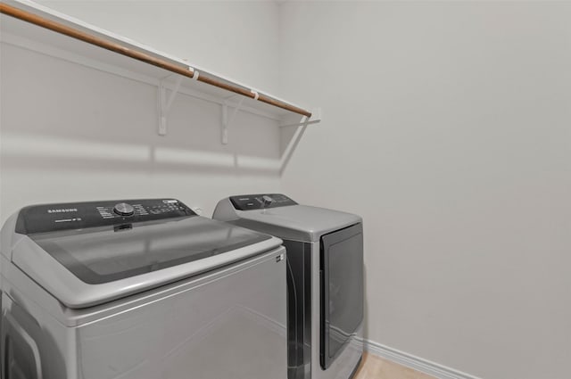 clothes washing area with washer and clothes dryer and light wood-type flooring