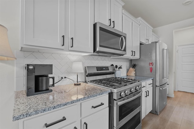 kitchen with light stone countertops, backsplash, light hardwood / wood-style floors, white cabinets, and appliances with stainless steel finishes