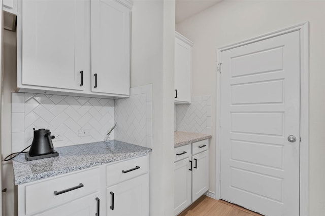 kitchen with light hardwood / wood-style floors, light stone counters, white cabinetry, and backsplash