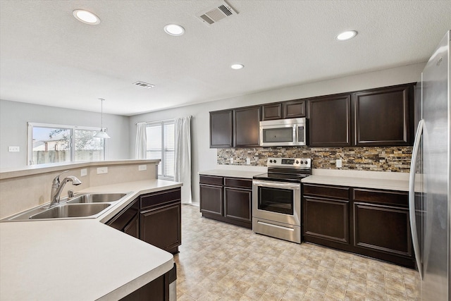 kitchen with pendant lighting, backsplash, sink, dark brown cabinetry, and stainless steel appliances