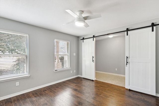 unfurnished room with ceiling fan, a barn door, and dark wood-type flooring