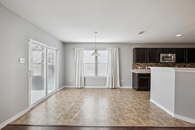 kitchen with tasteful backsplash, a healthy amount of sunlight, dark brown cabinets, and pendant lighting