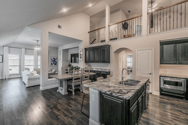 kitchen featuring sink, light stone counters, dark hardwood / wood-style flooring, high vaulted ceiling, and an island with sink