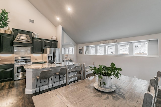 kitchen featuring a kitchen bar, appliances with stainless steel finishes, backsplash, custom range hood, and a kitchen island