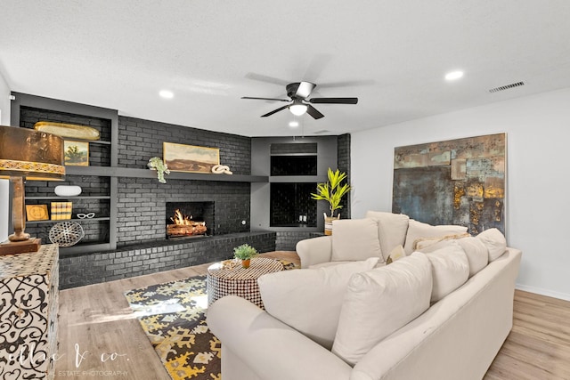 living room featuring a textured ceiling, a brick fireplace, built in features, light wood-type flooring, and ceiling fan