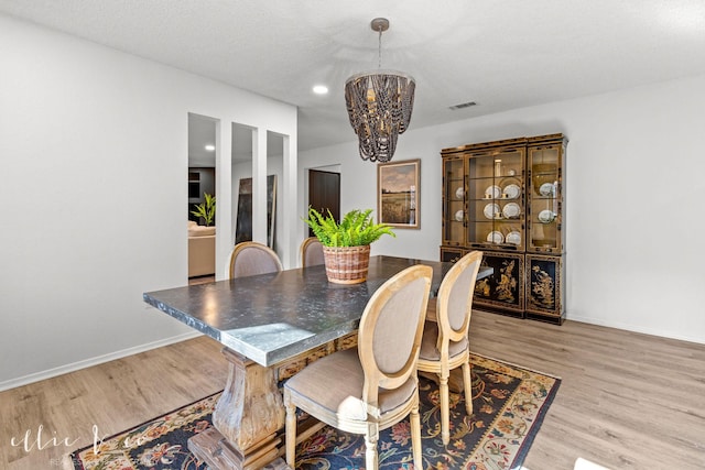 dining room featuring light hardwood / wood-style floors, a textured ceiling, and a notable chandelier