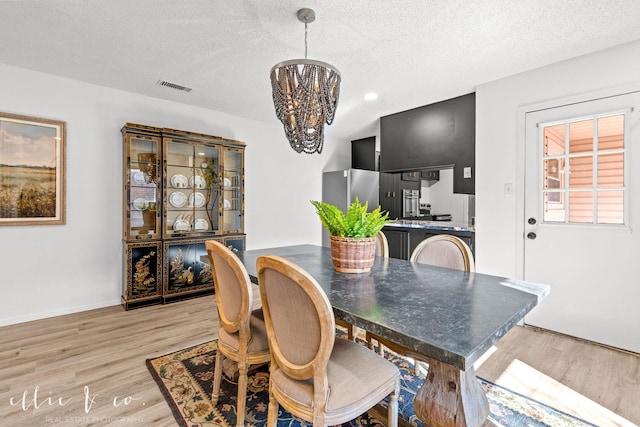 dining room featuring a notable chandelier, light wood-type flooring, and a textured ceiling