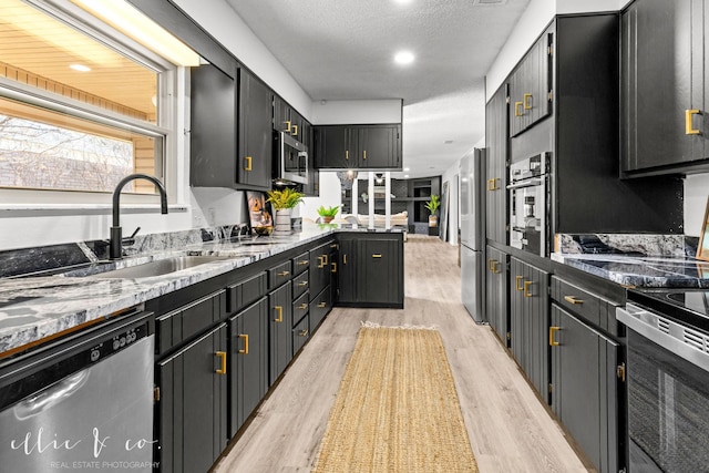 kitchen with a textured ceiling, appliances with stainless steel finishes, dark stone counters, light hardwood / wood-style floors, and sink